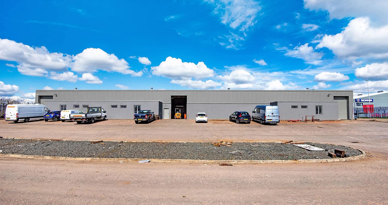Front elevation of industrial unit at Blocks 11 and 12, Nobel Road, Wester Gourdie Industrial Estate, with parking area, vehicles, and central access point.