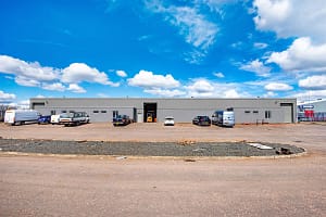 Front elevation of industrial unit at Blocks 11 and 12, Nobel Road, Wester Gourdie Industrial Estate, with parking area, vehicles, and central access point.